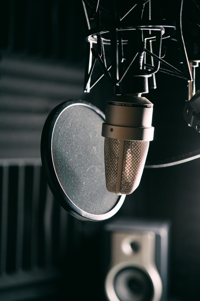 Detailed close-up of a studio microphone and pop filter in a dimly lit recording studio.