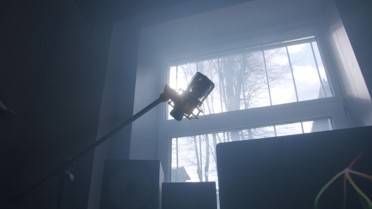 A microphone setup in a recording studio with sunlight streaming through a window.
