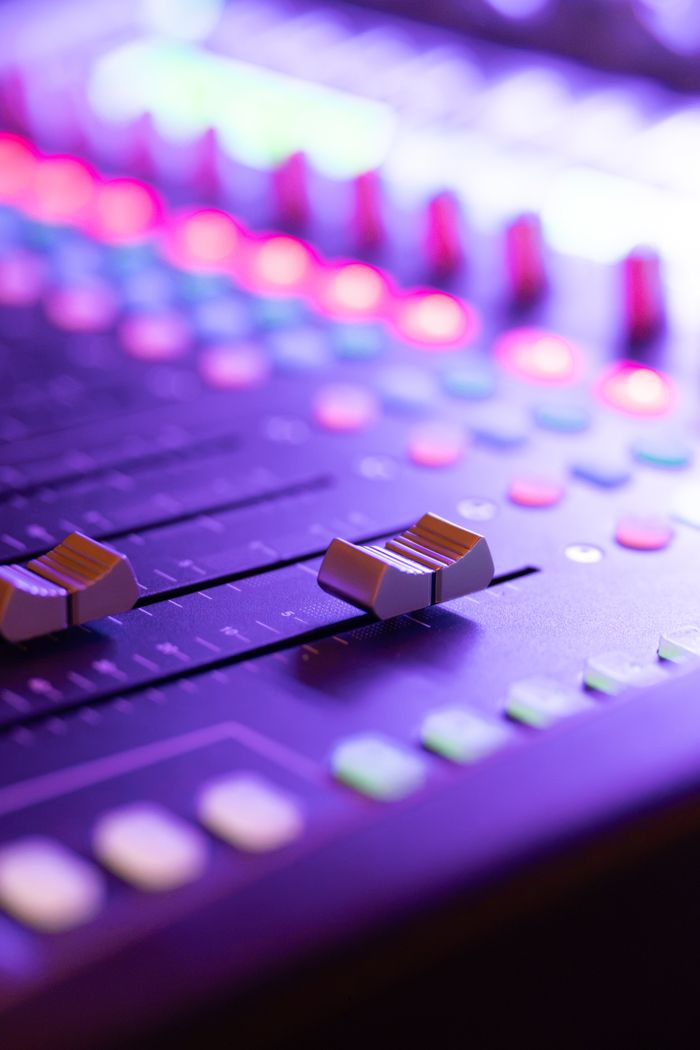 Vibrant close-up of an illuminated audio mixing console at night, showcasing control knobs and sliders.